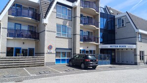 Un edificio de varios pisos con balcones, un coche estacionado adelante y un cartel que indica prohibido estacionar.