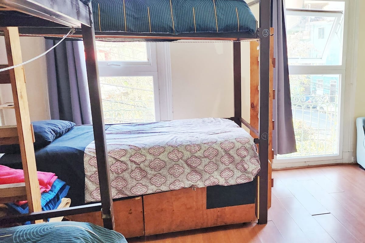 A room with a wooden four-poster bed, a green sofa, and a window with a view of the outside.