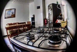 A kitchen with a gas stove, a refrigerator, and a dining area with chairs. - La Casa Piola (Valparaiso)