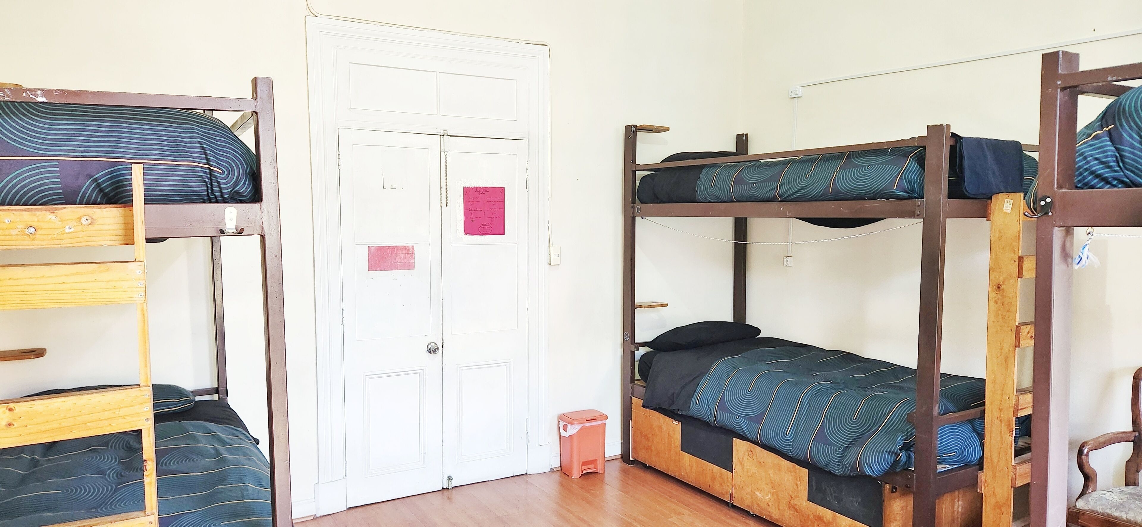A dormitory room with bunk beds, a white door, and a small trash bin.
