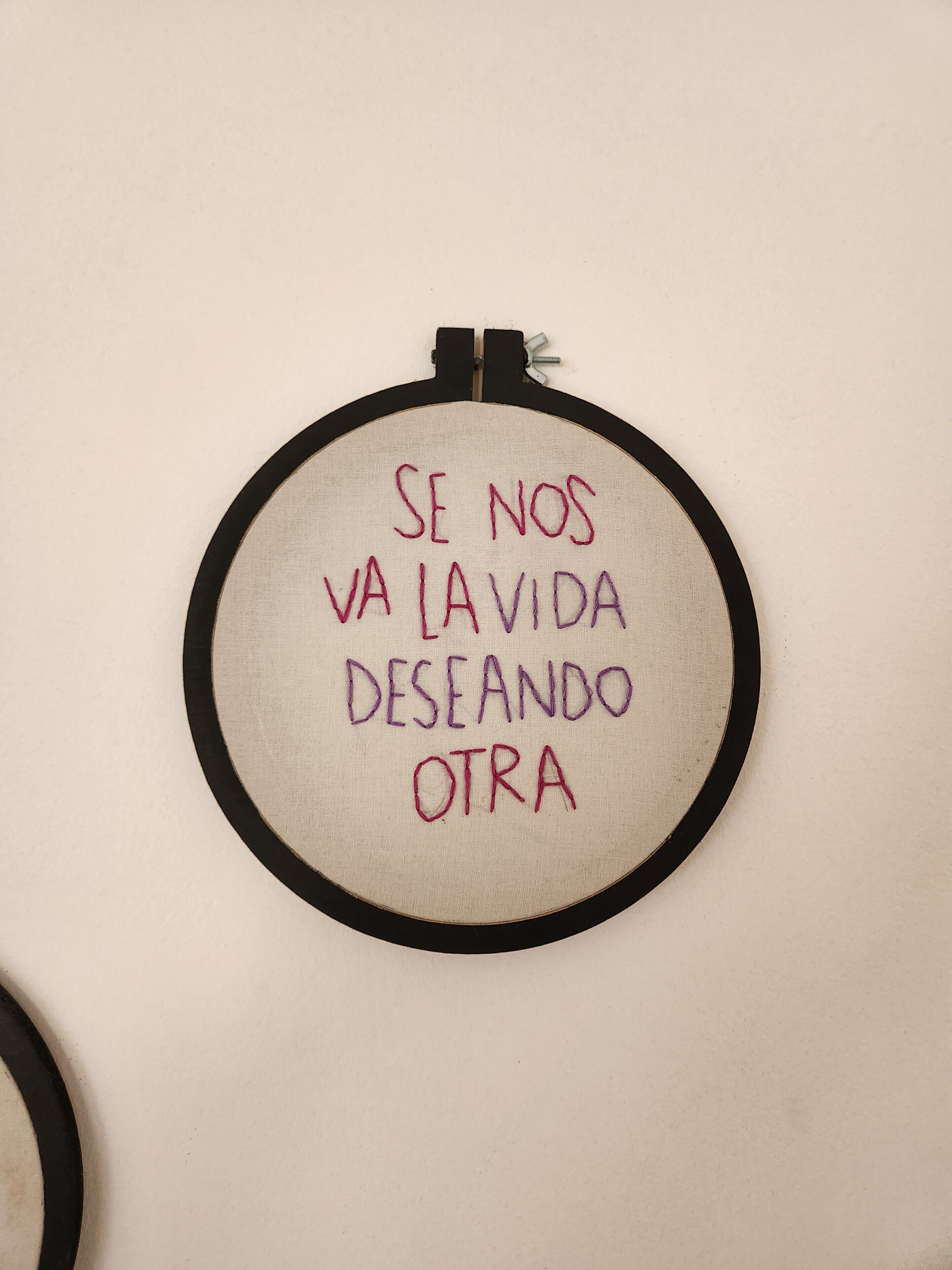 A circular embroidery with text on a beige background, framed by a black border.