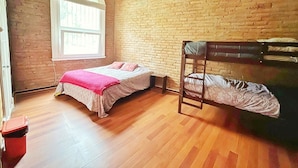 A room with a bunk bed, a single bed with a pink blanket, a window with white frames, and a brick wall. - La Casa Piola (Valparaiso)