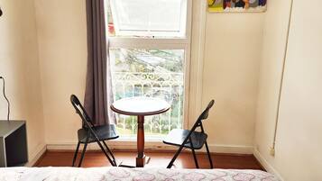 Une pièce comprenant un lit, une petite table, deux chaises, une fenêtre donnant sur un balcon et une prise électrique au mur.