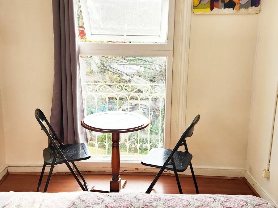 Une pièce comprenant un lit, une petite table, deux chaises, une fenêtre donnant sur un balcon et une prise électrique au mur.