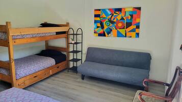 A room with bunk beds, a sofa, a chair, and a colorful abstract painting on the wall.