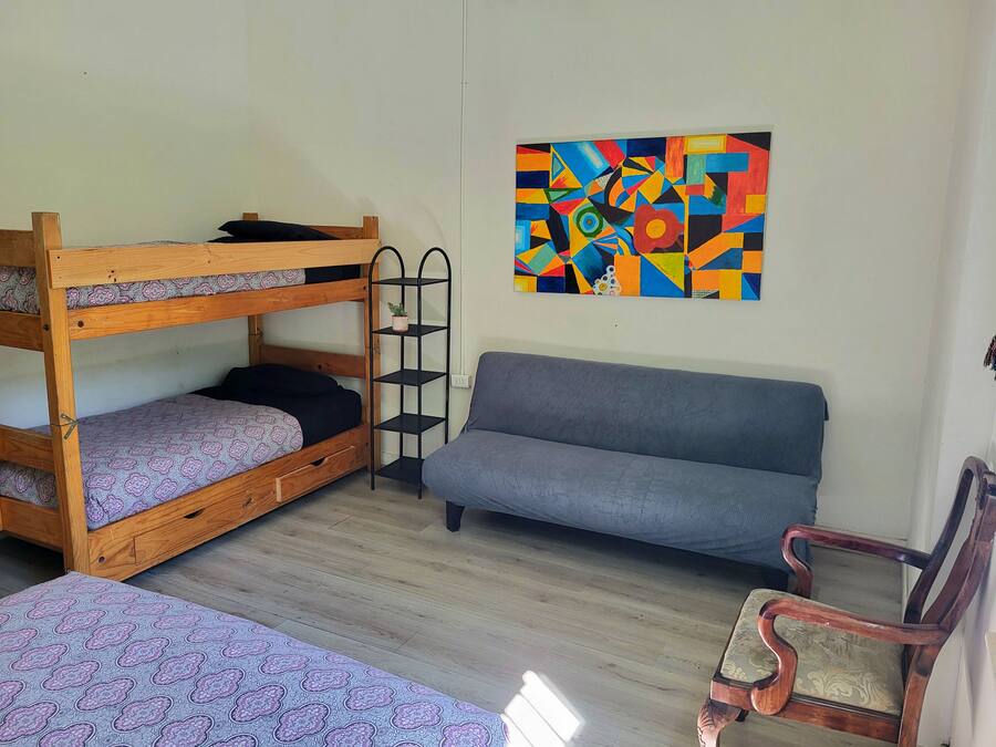 A room with bunk beds, a sofa, a chair, and a colorful abstract painting on the wall.