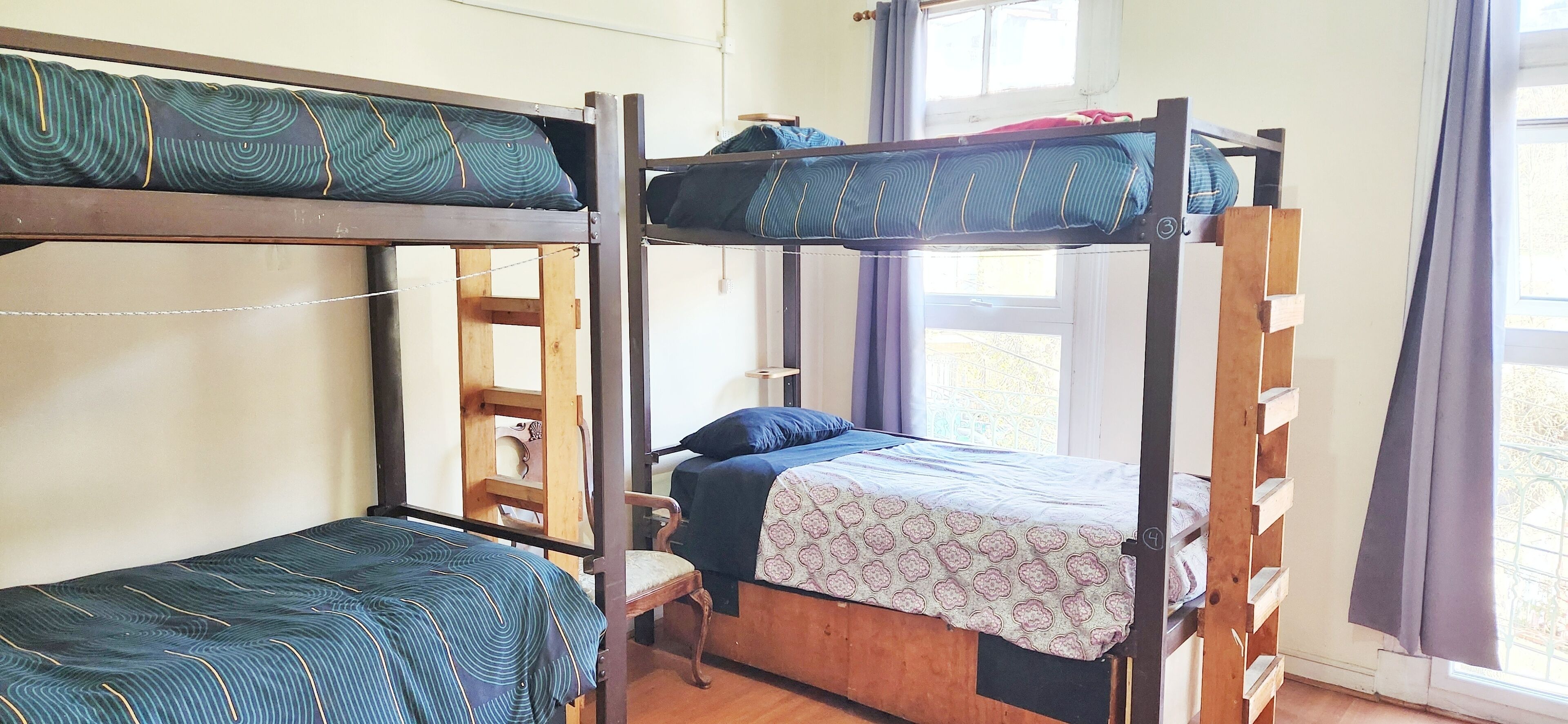 Ein Schlafsaalzimmer mit Etagenbetten, einer Holzleiter und einem Fenster mit Vorhängen.