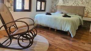 Een slaapkamer met een bed, een schommelstoel, twee ramen en bloemenbehang.
