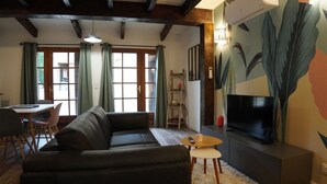 Een woonkamer met een hoekbank, een televisie en een open haard. Er is een eethoek met een tafel en stoelen.