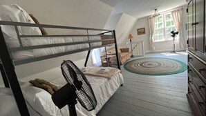 Habitación con literas, un ventilador de pie, suelo de madera, cómoda y ventana con cortinas.