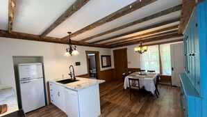 Una cocina con vigas de madera, un refrigerador, un lavamanos y un comedor con una mesa y sillas.