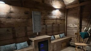 Interior de una cabaña de madera con un banco, una silla y una pequeña mesa con televisor.