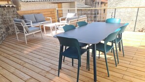 A wooden deck with a table and chairs, a sofa, and a stone wall. - La Maison du Vieux Bourg (Perrier)