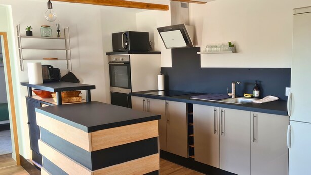 A modern kitchen with a black and wooden island, built-in oven, microwave, and a sink with a faucet. - La Maison du Vieux Bourg (Perrier)