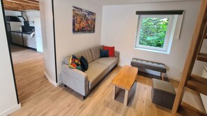 A modern living room with a sofa, a bench, a wooden coffee table, and a window with a view of greenery. - La Maison du Vieux Bourg (Perrier)
