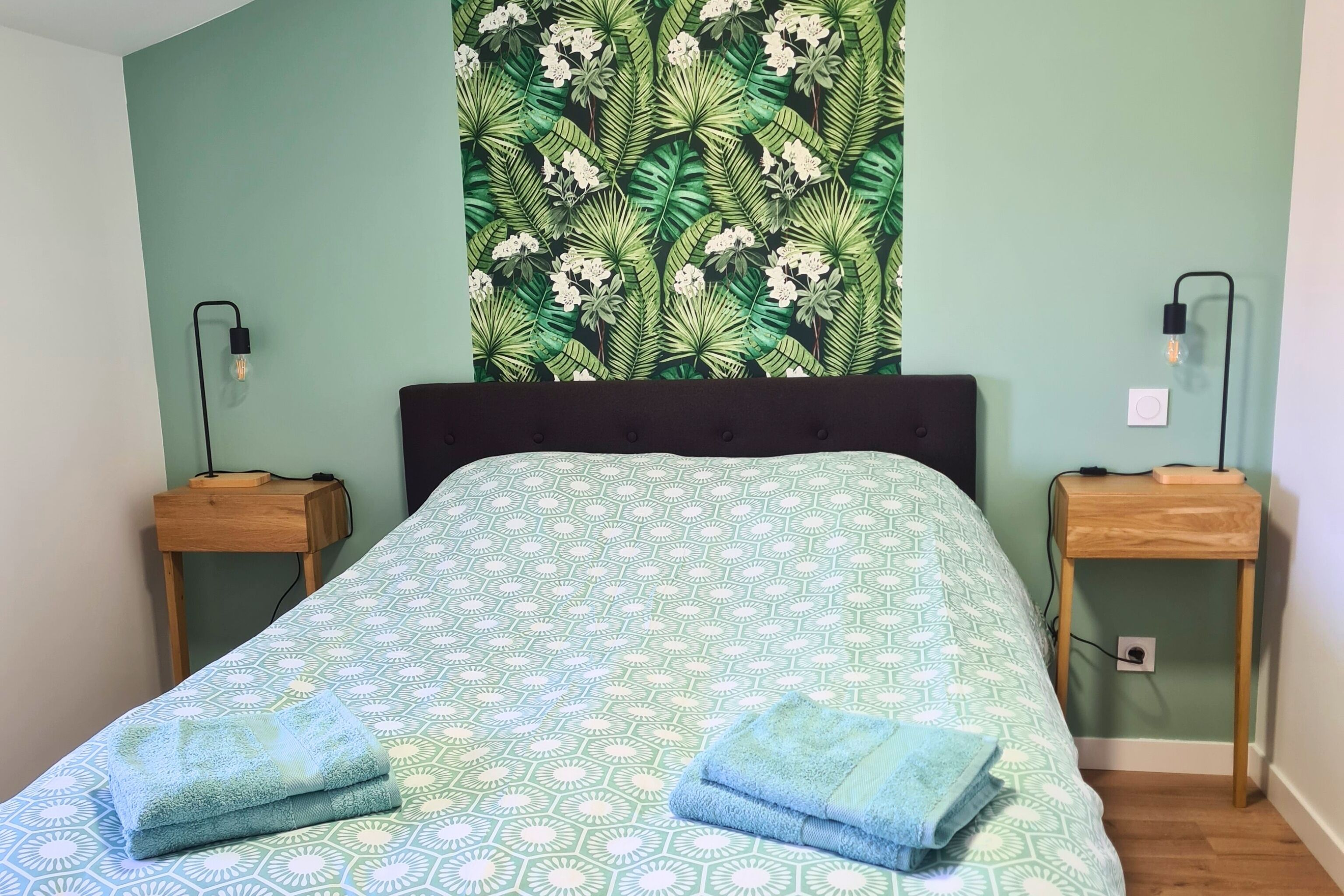 Een bed met een gebedekte spreideel, twee nachtkastjes en een wandtapijt.