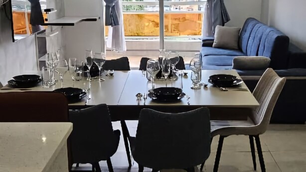 Een moderne woonkamer met een eethoek, een bank en een groot raam met gordijnen.