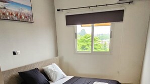 Een slaapkamer met een bed, een raam met uitzicht op groen en een airconditioning.
