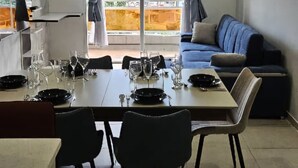 Een eetgedeelte met een tafel voor vier personen, een bank en uitzicht op gebouwen door een glazen deur.