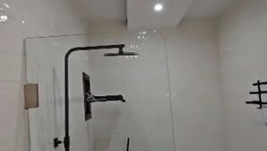 Een moderne badkamer met een douchecabine van glas, een zichtbare douchekop en een handdoekhouder aan de muur.