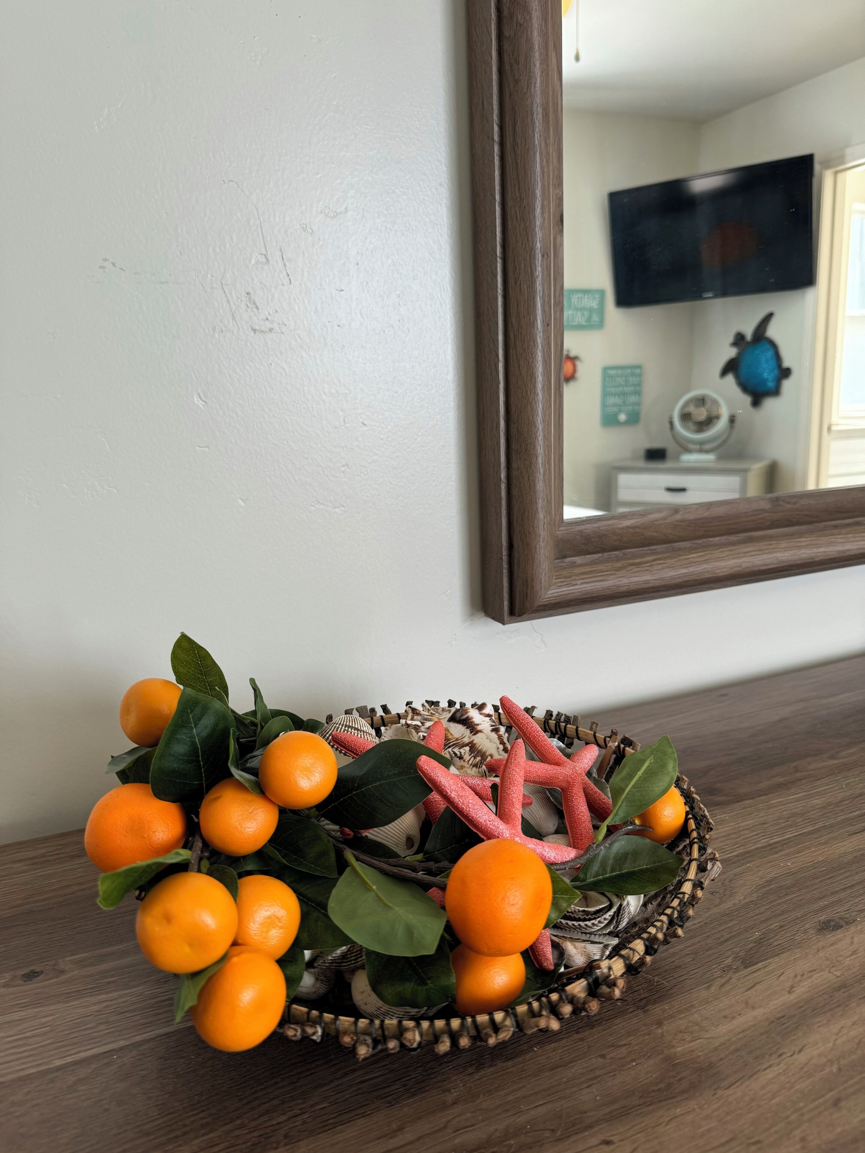 A wooden shelf with a woven basket containing oranges, green leaves, and a starfish.