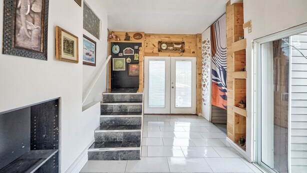 Un couloir avec un escalier menant à une porte, décoré de divers tableaux encadrés et d’une horloge.