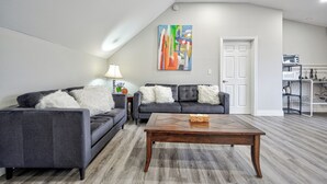 Un salon moderne avec deux canapés gris, une table basse en bois et un tableau abstrait aux couleurs vives accroché au mur.