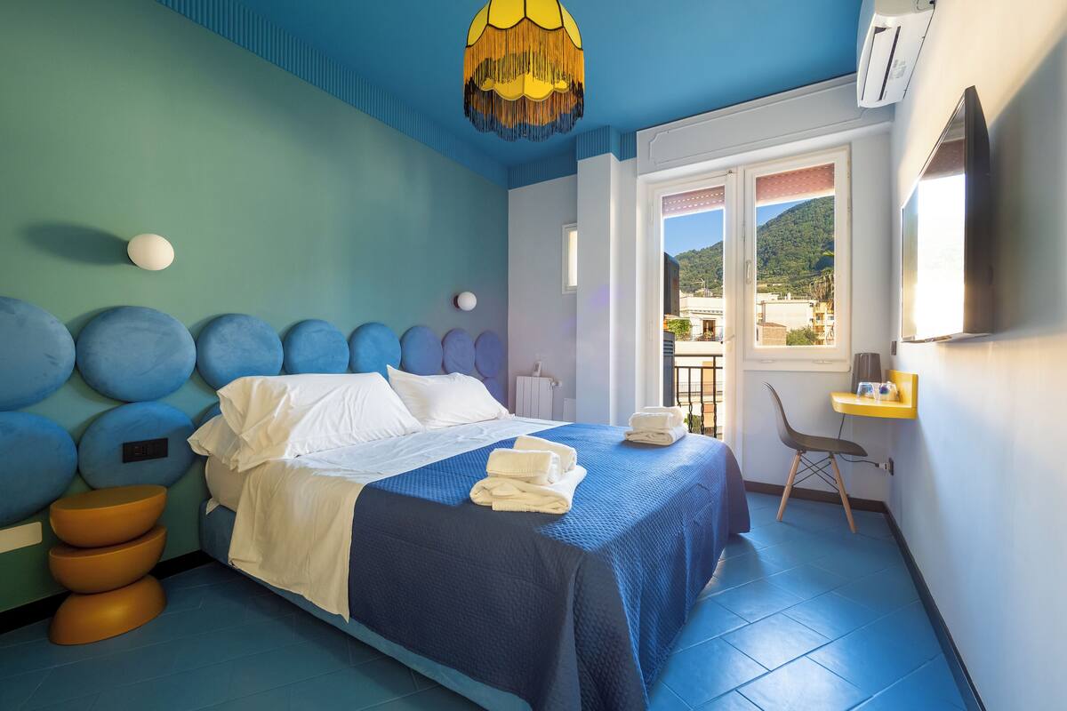 Een slaapkamer met een bed, een stoel, een klein tafeltje, een raam met uitzicht en een plafondlamp.