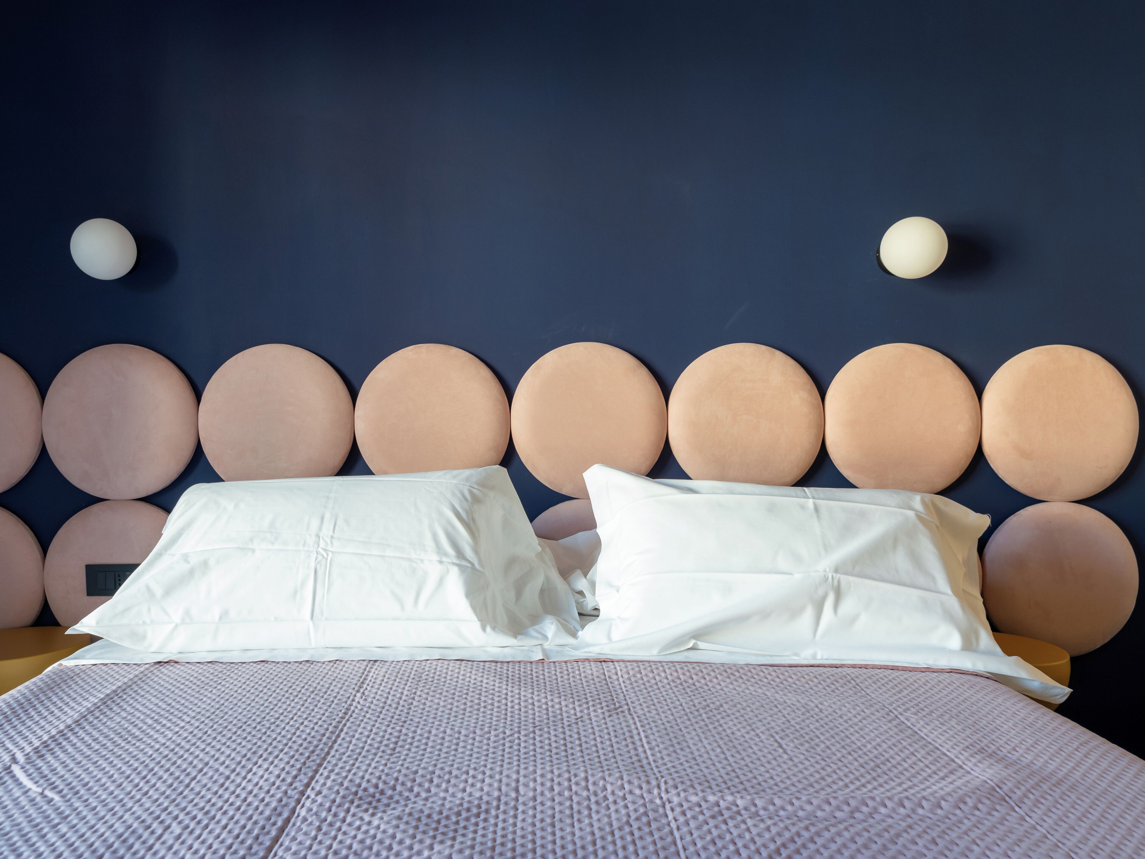 Een bed met een gebordureerd wit dekbed, twee witte kussens en een hoofdbord met ronde decoraties.