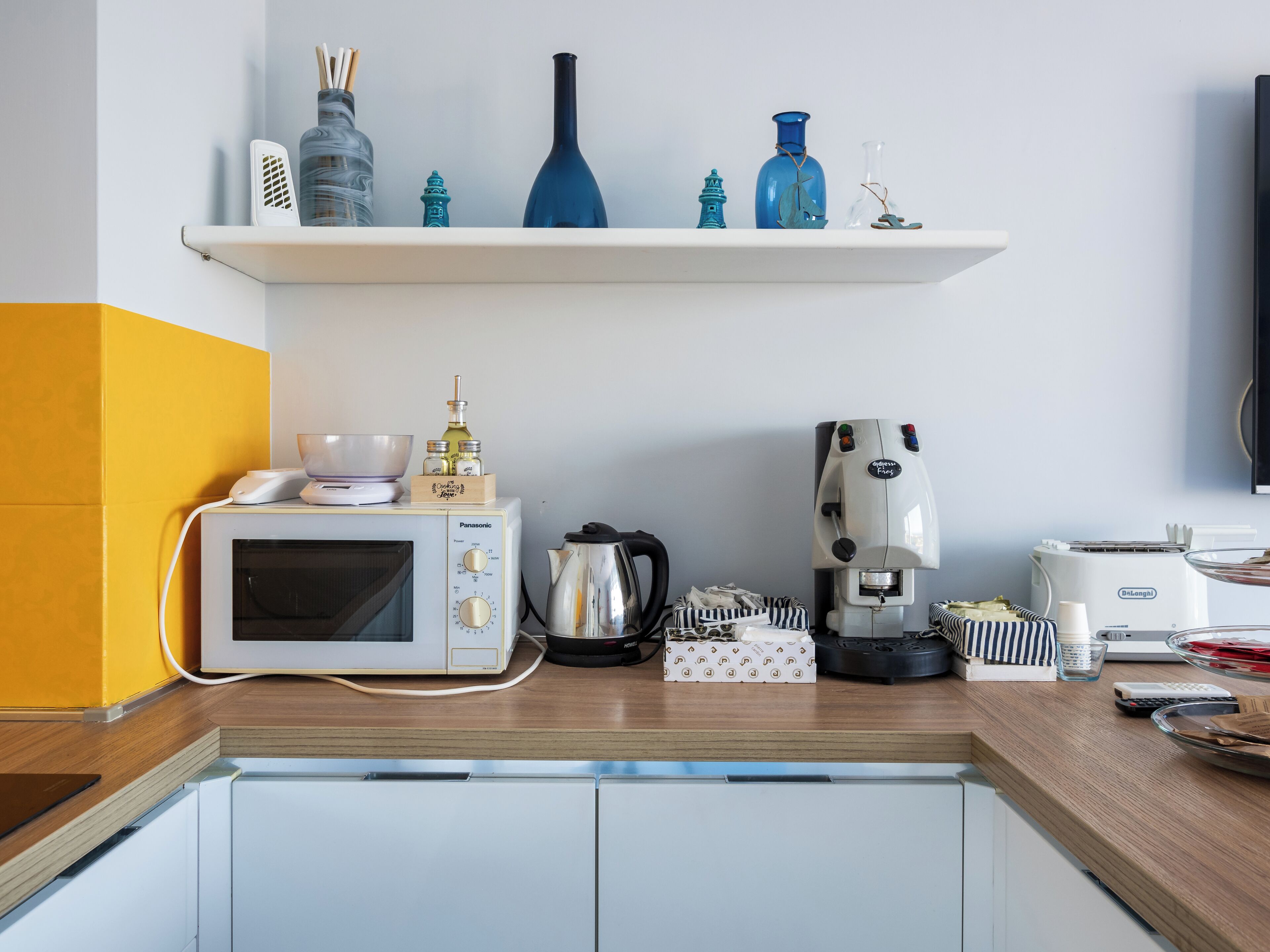Uma cozinha com micro-ondas, cafeteira e uma estante com objetos decorativos.