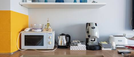 Uma cozinha com micro-ondas, cafeteira e uma estante com objetos decorativos.