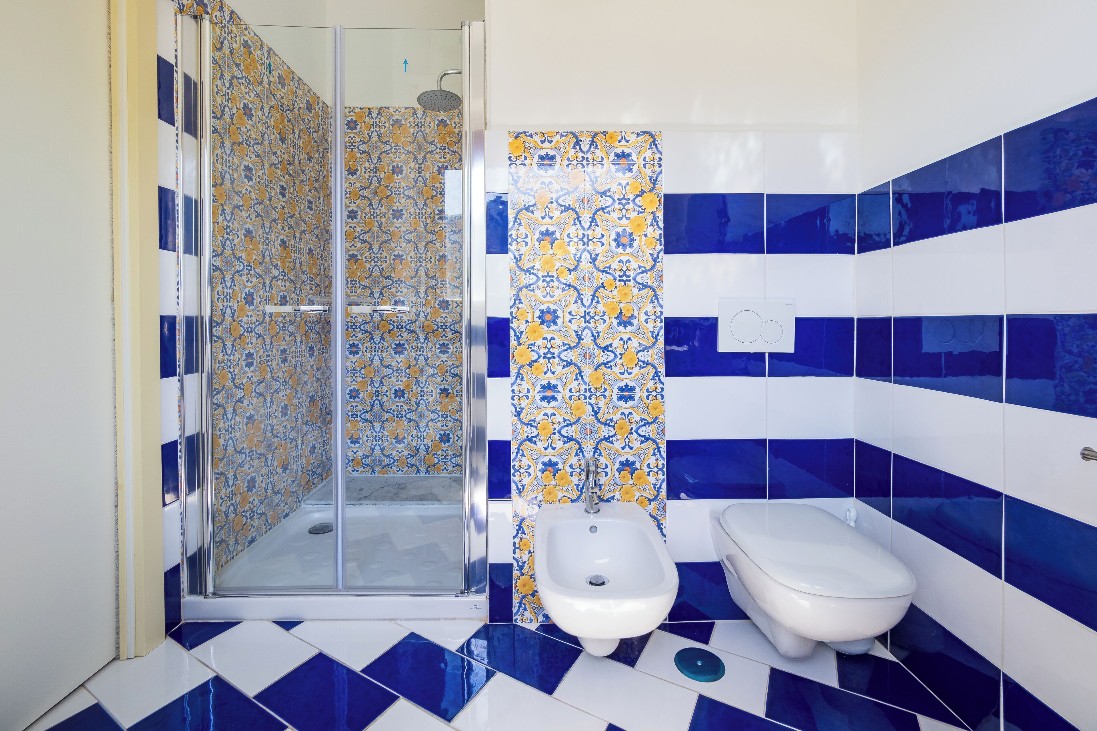 Un baño con ducha, bidé y paredes con azulejos azules y blancos.