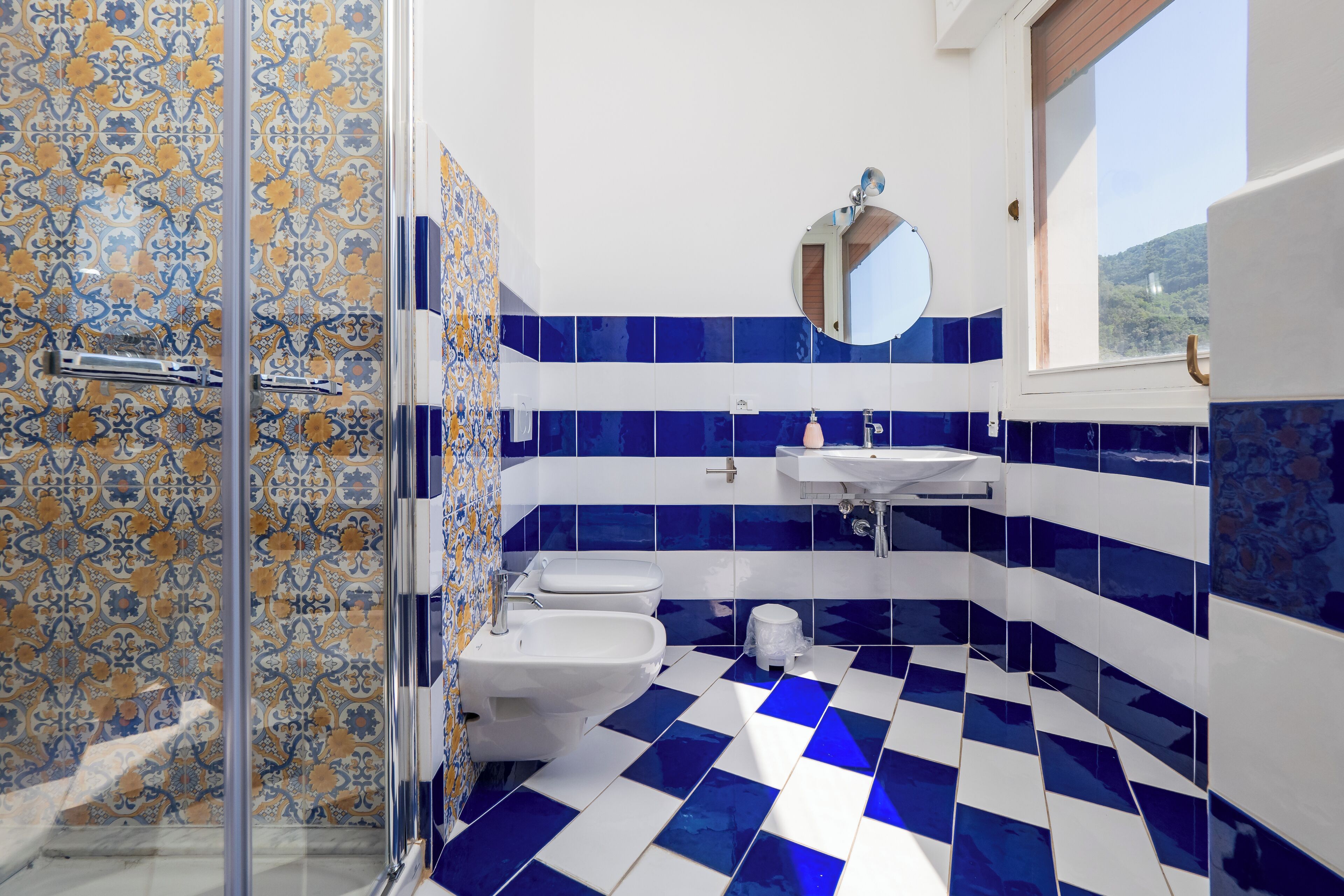A bathroom with patterned tiles, a glass shower enclosure, a sink, and a toilet.