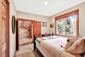 A bedroom with a large bed, a window with a view of trees, a wooden door, and a staircase leading to another room.