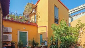 Un edificio amarillo con balcón, unidades de aire acondicionado y plantas en macetas.