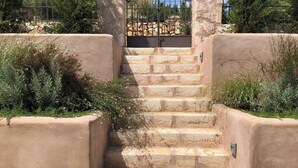 A set of stone steps leading up to a gated area, surrounded by greenery and a stone wall.