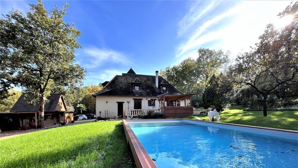 A swimming pool with a wooden deck, a house with a porch, and a grassy yard. - Chambre La Terrasse (Sarliac-sur-l'Isle)
