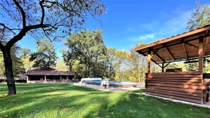 A covered outdoor area with a wooden deck, a pool, and a picnic shelter in a park. - Chambre La Terrasse (Sarliac-sur-l'Isle)