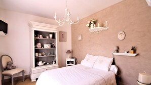 A bedroom with a large bed, a dresser, a chair, a nightstand, and a shelf with decorative items. - Chambre La Terrasse (Sarliac-sur-l'Isle)