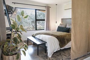 A bedroom with a bed, bedside table, lamp, and a view of trees through a window.