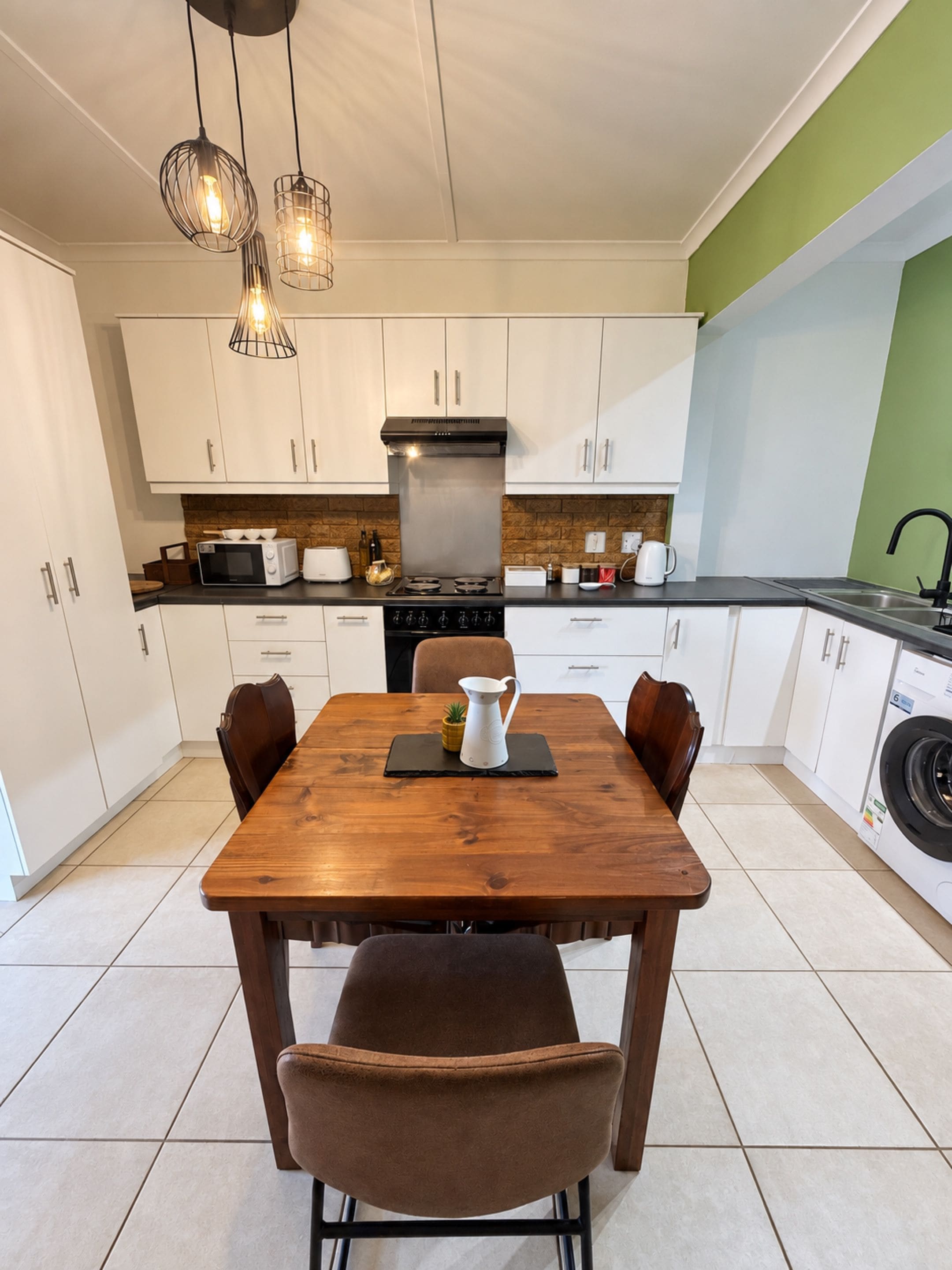 A modern kitchen with white cabinets, a wooden dining table, and a built-in washing machine.