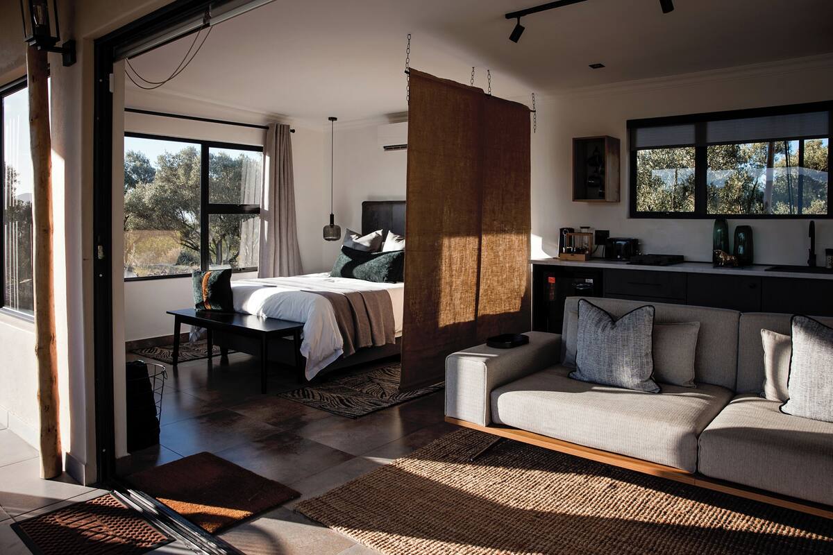 A modern bedroom with a large bed, a sofa, and a kitchen area.