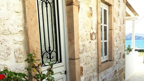 Un bâtiment en pierre avec une porte et une fenêtre blanches, un chemin pavé de pierres et une vue sur la mer.