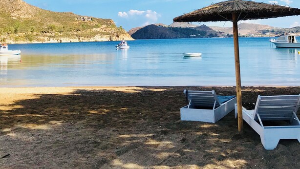 Une plage avec des chaises longues, un parasol en chaume et des bateaux sur une eau calme.