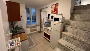 Une cuisine compacte équipée d’un four à micro-ondes, d’une machine à café et d’un petit réfrigérateur. Un escalier mène à un balcon offrant une vue sur l’extérieur.