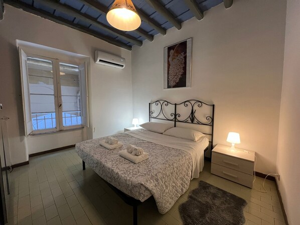 A bedroom with a bed, a nightstand, a lamp, an air conditioner, and a window.