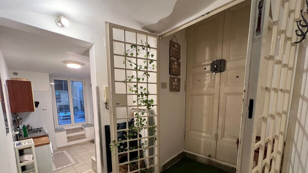 Une pièce dotée d’une porte coulissante donnant sur un balcon, d’un coin cuisine avec un évier et des placards, et d’un petit hall d’entrée avec un paillasson.