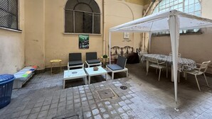 Une cour dotée d’un espace salon abrité, d’une table et de chaises. On y trouve deux petites tables et un banc.