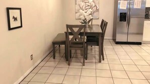 Un coin repas avec une table et des chaises, un lustre, un réfrigérateur et un tableau encadré au mur.