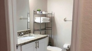 Une petite salle de bain avec un lavabo blanc, un plan de travail et une étagère en métal au-dessus.